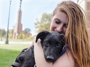 Girl hugs a black labrador dog outside