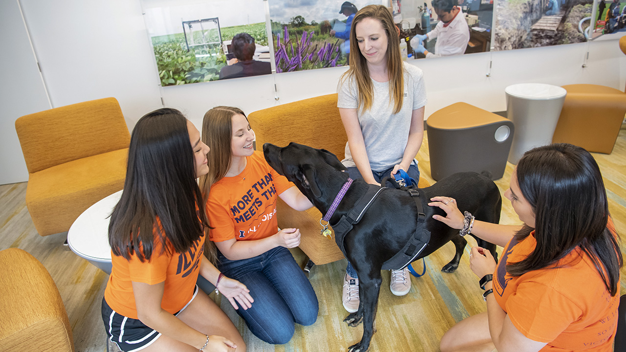 Group of students gathered around a black labrador dog.