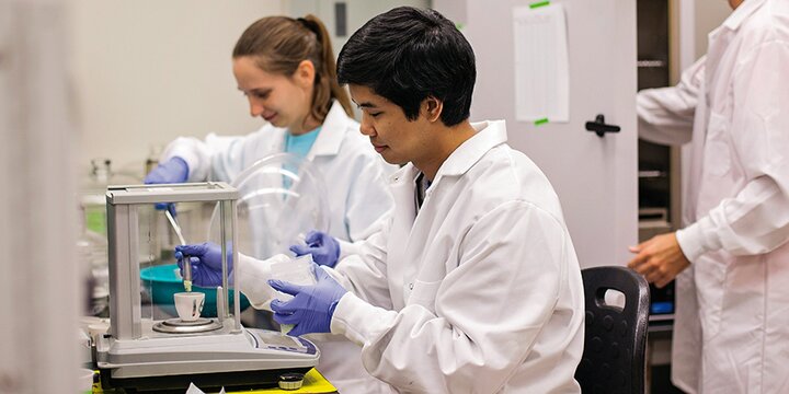 Students in lab coats working in lab.
