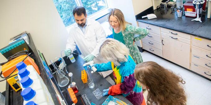 Students in lab coats working in lab.