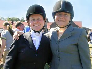 Two girls in horseback riding apparel standing outside