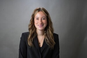 A female in black blazer with gray background.
